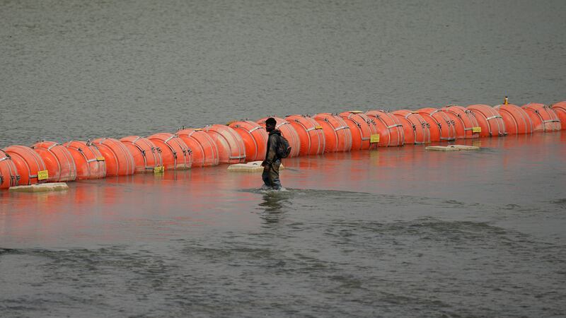 A migrant from Columbia walks along a floating buoy barrier as he looks to cross the Rio...
